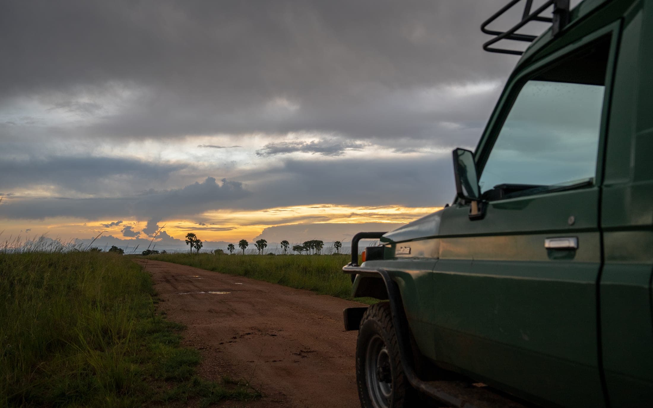 A safari vehicle on a Ugandan track at golden hour